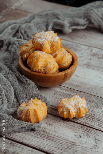 Delicious homemade cakes and desserts. Cream profitroles with sugar powder on plate on white wooden background photo