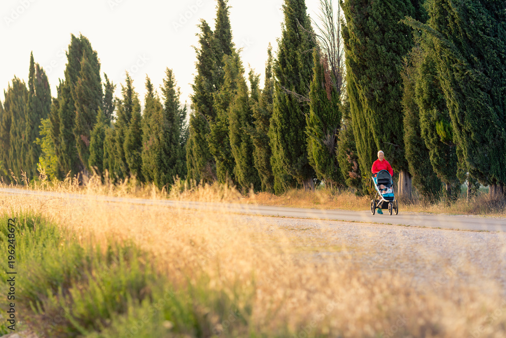 Running mother with baby stroller enjoying sunset landscape Running mother with baby stroller enjoying sunset landscape