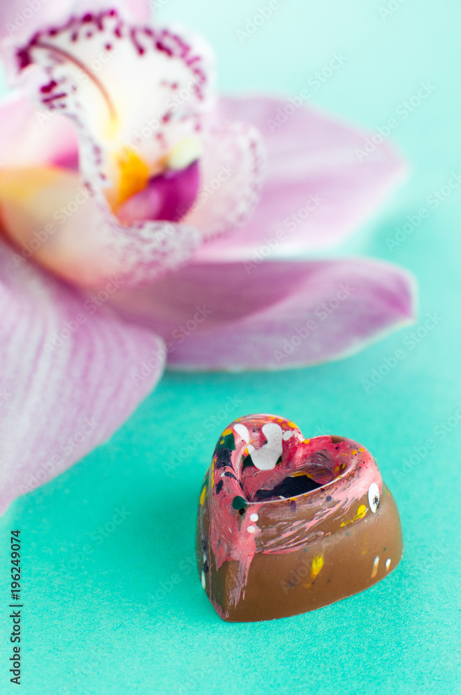 Closeup view of chocolate heart shape candy near orchid flower Closeup view of chocolate heart shape candy near orchid flower