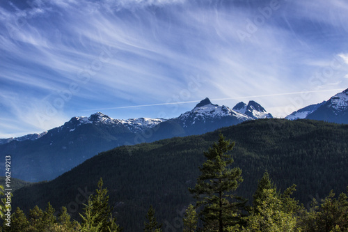 wispy clouds, mountain peaks and a forest