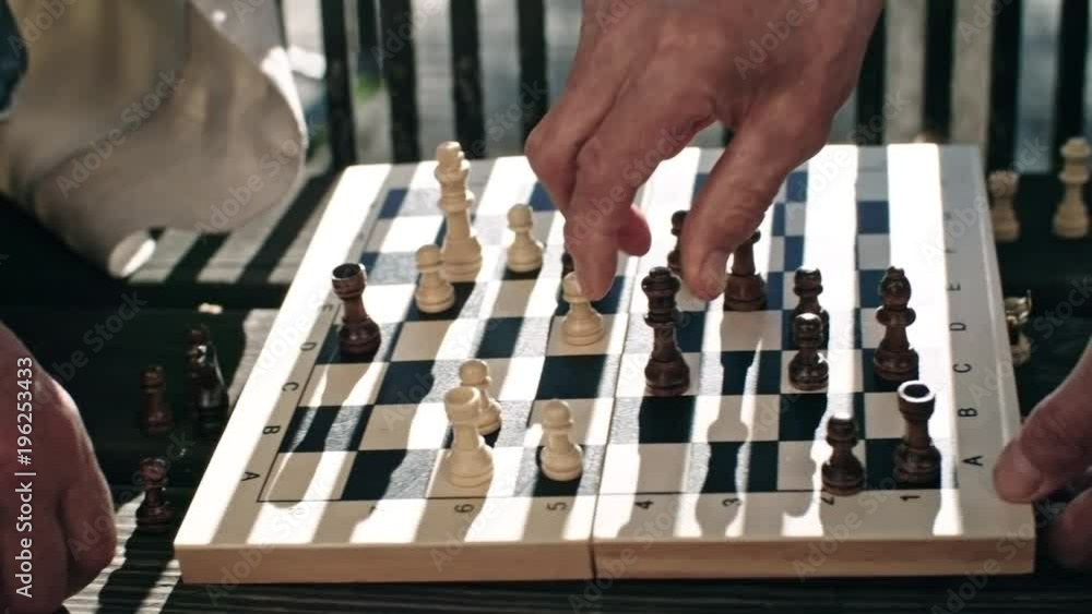 Close up hands of two senior men playing chess on bench in park, tracking shot Close up hands of two senior men playing chess on bench in park, tracking shot