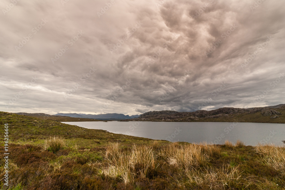 Loch Tollaidh, Scotland - June 9, 2012: Heavy dark brown cloudscape over lake colors water dark. Set between rocky mountains. Green grass in front. Wide landscape shot. Loch Tollaidh, Scotland - June 9, 2012: Heavy dark brown cloudscape over lake colors water dark. Set between rocky mountains. Green grass in front. Wide landscape shot.