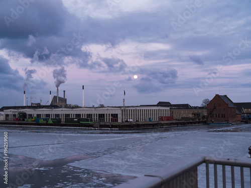 Frozen harbor with industry buildings sneding smoke up in a dramtic sky © Christoffer