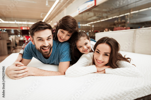 Little children lie on the backs of young happy parents in a mattress store. photo