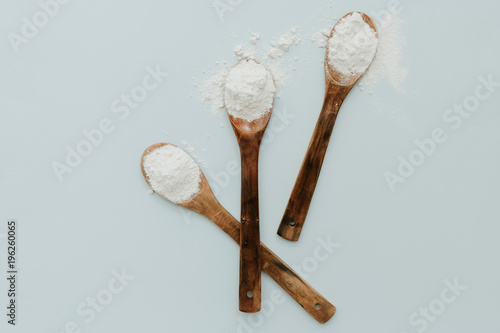 Wooden spoon with flour on pastel background. Top view, flat lay