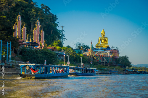 Gorgeous view of a group of tourists visiting in tourist boats the golden budha located at golden triangle Laos with some building in the riverbank photo