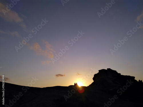 Couple - man and woman silhouette at the top of the mountain in front of sunset. Hiker rest on the rock. Background with copyspace. Symbol of romance, motivation, success, achievement