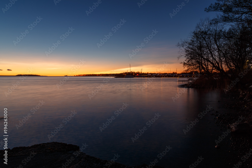 sunset at a lake with trees on the side and boats on the horizon