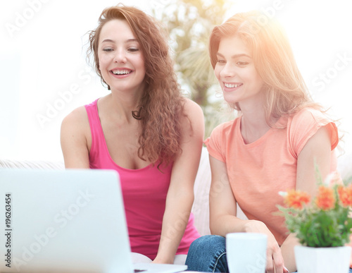 two student girls looking at laptop screen while sitting on the couch.