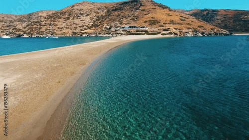 Crystal clear water of mediterranean Aegean sea and sandy coast line of Kolona beach of Kythnos island. Slow movement over surface towards the mountain with rocks and arid bushes. Kythnos, Greece
