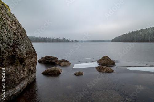 ice and stones at a small lake with forest all around