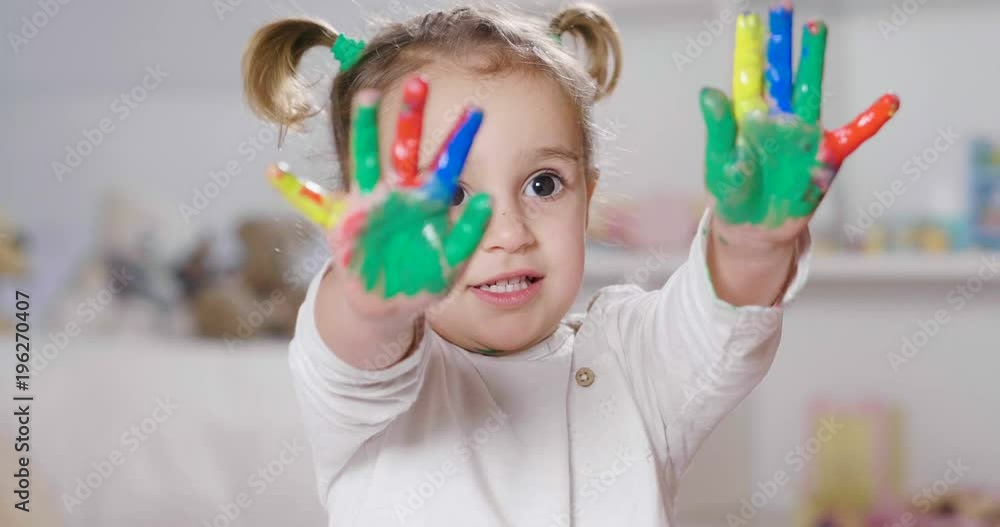 Portrait of a little girl in her bedroom showing her hands all colored with paint. Concept of: color, creativity, art, happiness and educational. Portrait of a little girl in her bedroom showing her hands all colored with paint. Concept of: color, creativity, art, happiness and educational.
