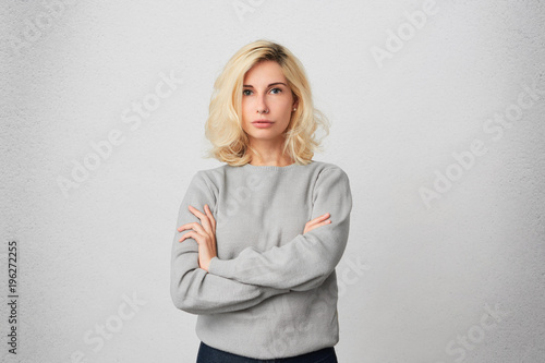 Young blonde girl with pierced nose looking directly into camera and worried about problems with her boyfriend. Isolated over white wall