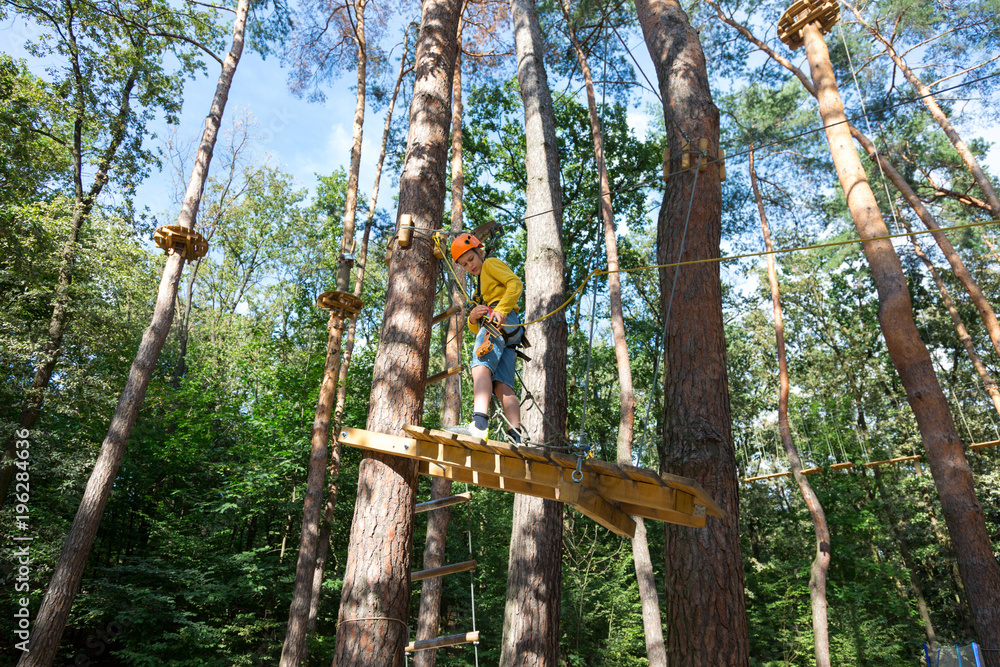 Fototapeta premium adventure climbing high wire park - boy on course in mountain helmet and safety equipment