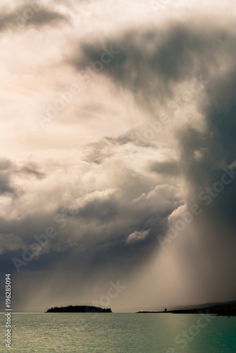 Moody, dramatic storm clouds over island on Lake Tekapo, New Zealand.