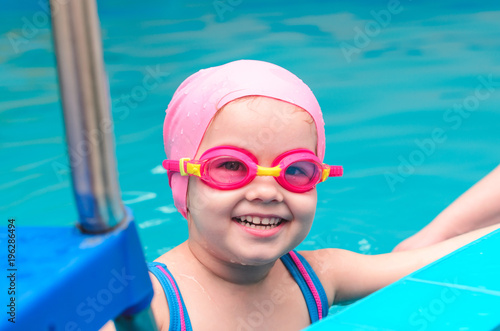 A little girl of European appearance in a pink rubber cap learning to swim in the pool in glasses for swimming © Maksim