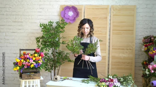 Florist at work: pretty young blond woman holds fashion modern bouquet of different flowers with peone and roses in craft paper photo