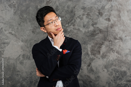 Portrait of a pensive young asian man dressed in suit thinking