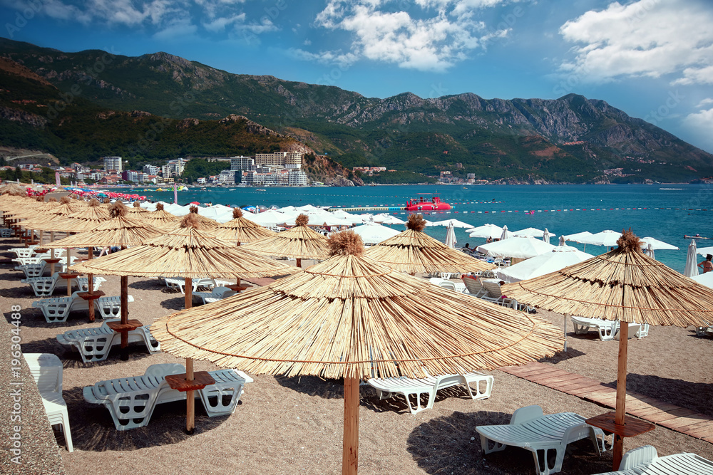 Chairs on the sandy beautiful beach and straw umbrella near the sea. Symbol of holiday vacation. Beach in Montenegro.