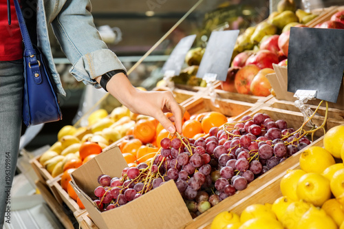 Young woman choosing fresh grapes in supermarket