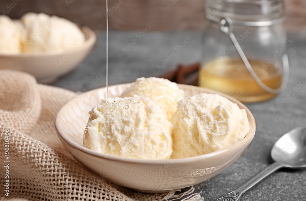 Pouring honey onto delicious vanilla ice cream in bowl on table