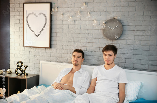 Young gay couple lying in b...