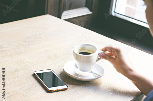 Close-up of mobile phone in woman's hands, sitting with cup of coffee.