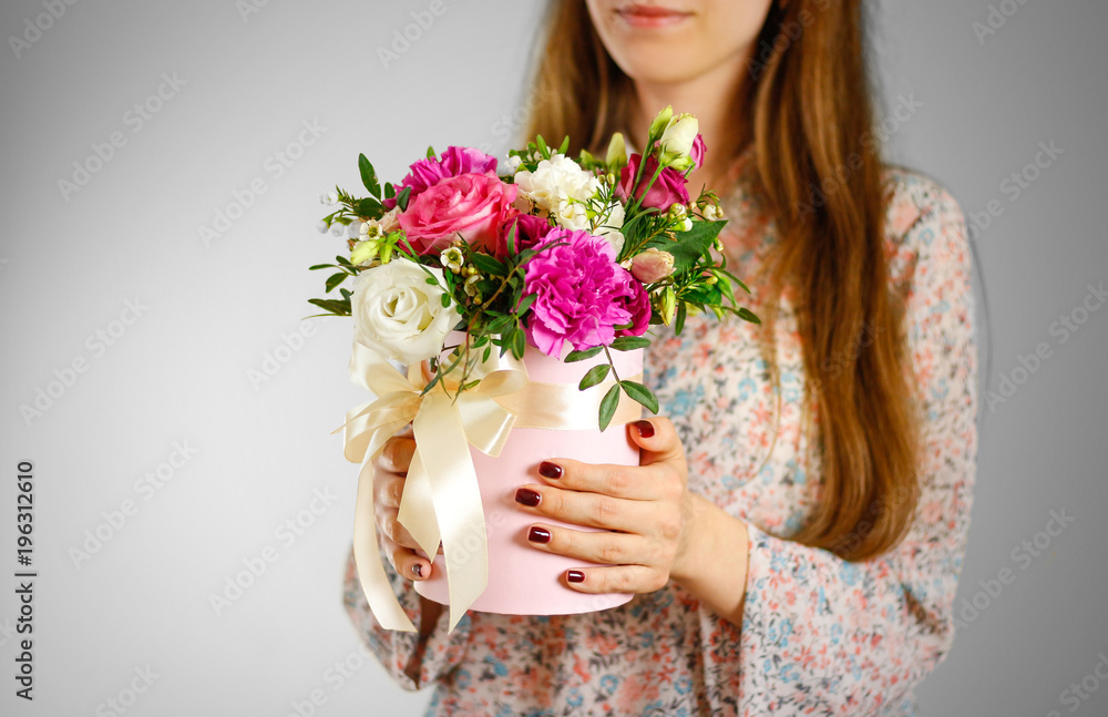 Girl holding in hand rich gift bouquet. Composition of flowers in a pink hatbox. Tied with wide white ribbon and bow Girl holding in hand rich gift bouquet. Composition of flowers in a pink hatbox. Tied with wide white ribbon and bow
