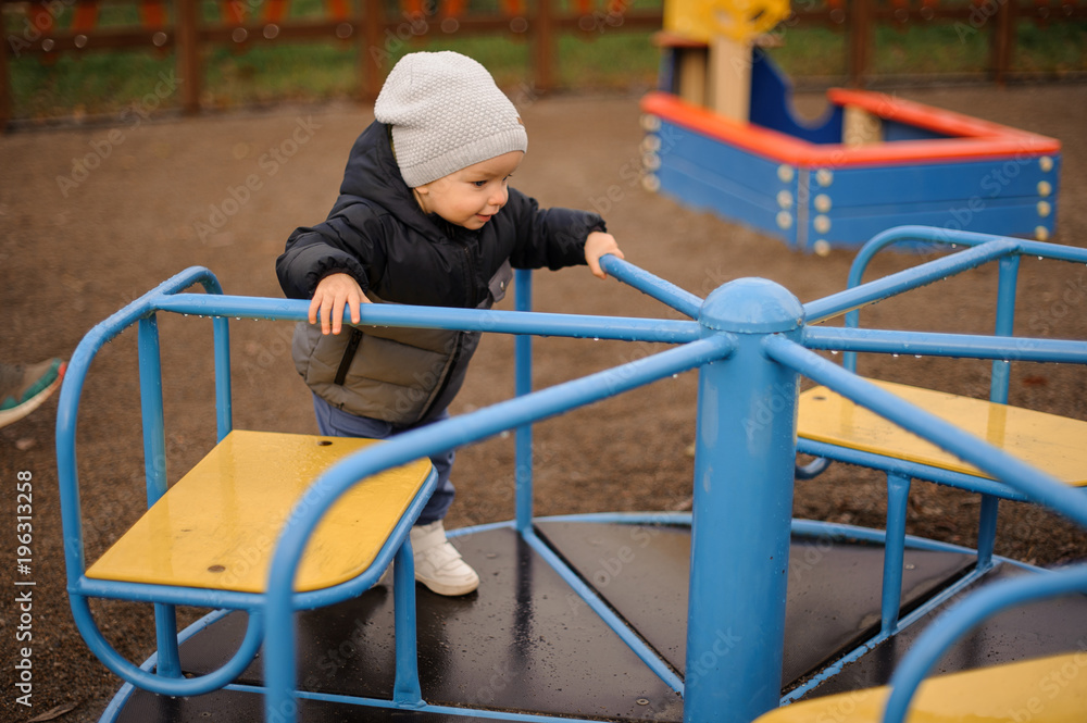 Cute little boy dressed in a warm hat and jacket riding on the carousel