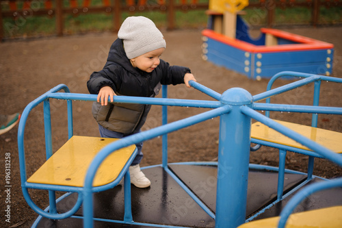 Cute little boy dressed in a warm hat and jacket riding on the carousel © fesenko