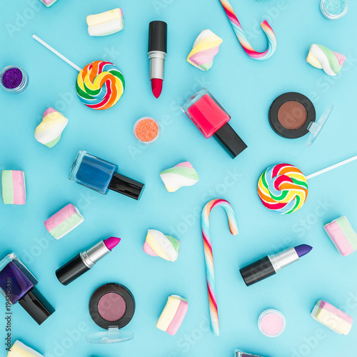 Composition with female cosmetics and bright candy on blue background. Top view. Flat lay. Creativity feminine desk.