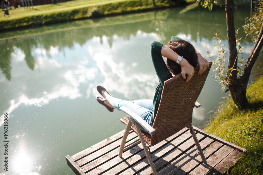 Young woman sitting on chair and relax on the lake coast in the park