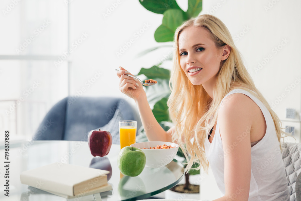 beautiful young woman eating muesli for breakfast and smiling at camera at home beautiful young woman eating muesli for breakfast and smiling at camera at home