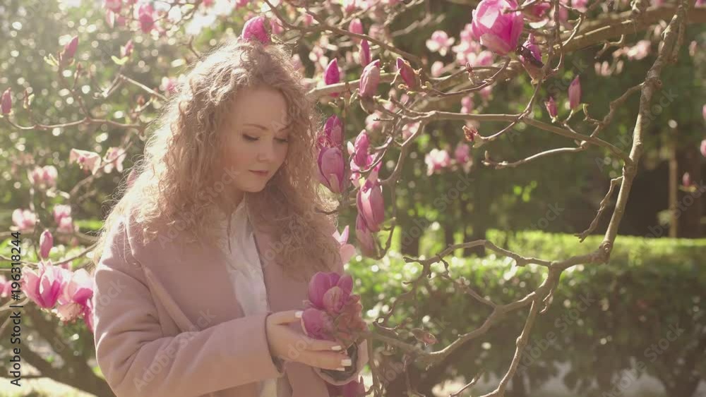 Young charming girl enjoys the pleasant scent of a blooming magnolia Young charming girl enjoys the pleasant scent of a blooming magnolia