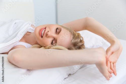 beautiful smiling blonde girl stretching and waking up in bed