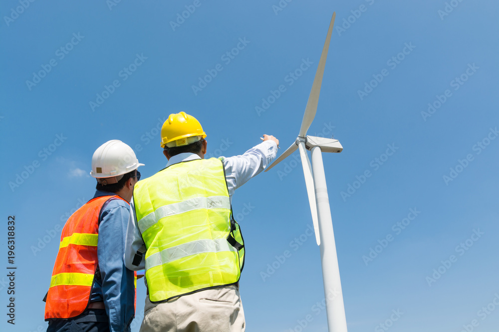 Engineer and Architect discuss over Digital Wireless Tablet and Clipboard while working at Wind Turbine Power Generator. Engineer and Architect discuss over Digital Wireless Tablet and Clipboard while working at Wind Turbine Power Generator.