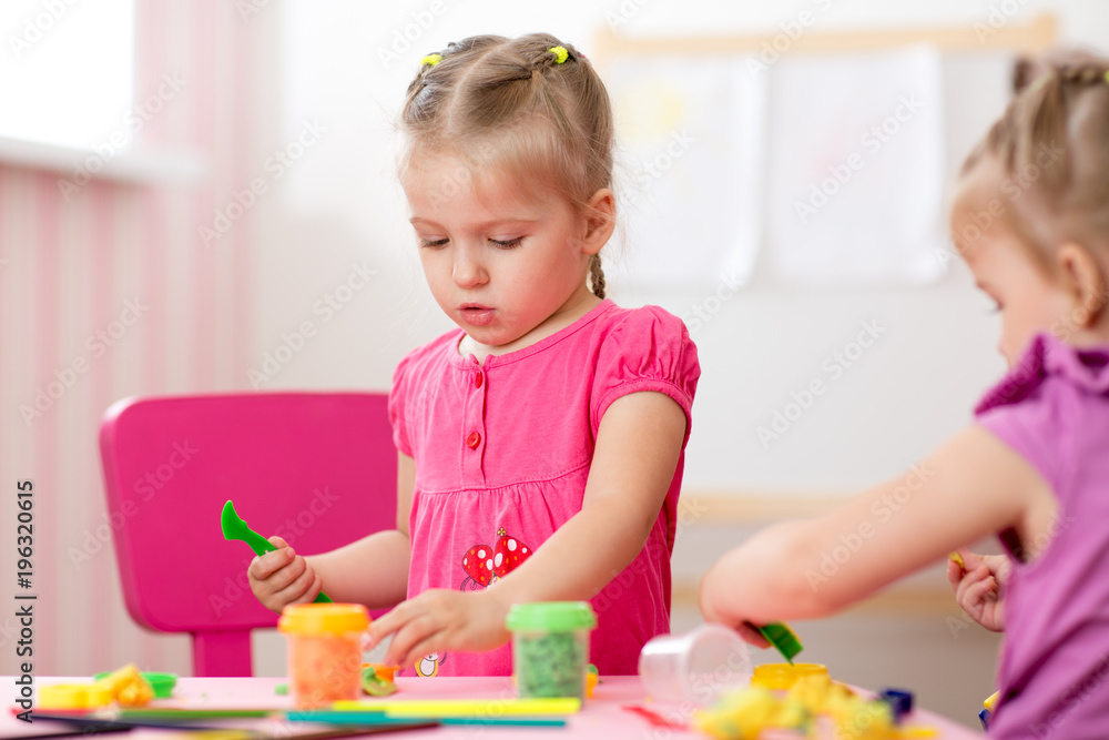 Children creativity. Kids sculpts from play clay. Cute little girl moulds from plasticine on table in nursery Children creativity. Kids sculpts from play clay. Cute little girl moulds from plasticine on table in nursery