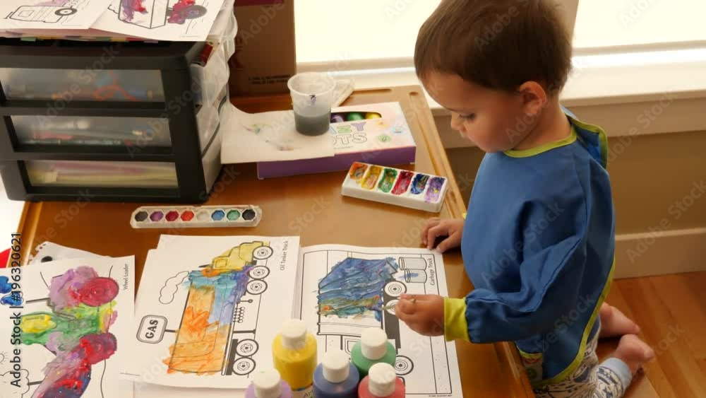 A cute little boy painting tractors at a craft table A cute little boy painting tractors at a craft table