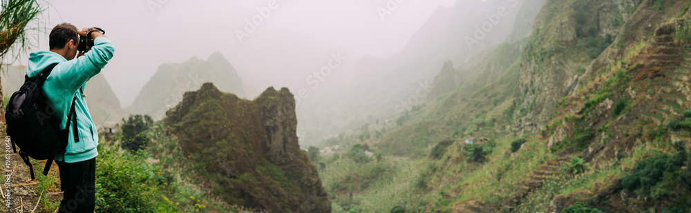 Traveler holding up the camera to take a photo of amazing steep mountainous terrain with lush canyon valley on the path from Xo-Xo Valley. Santo Antao Island, Cape Verde