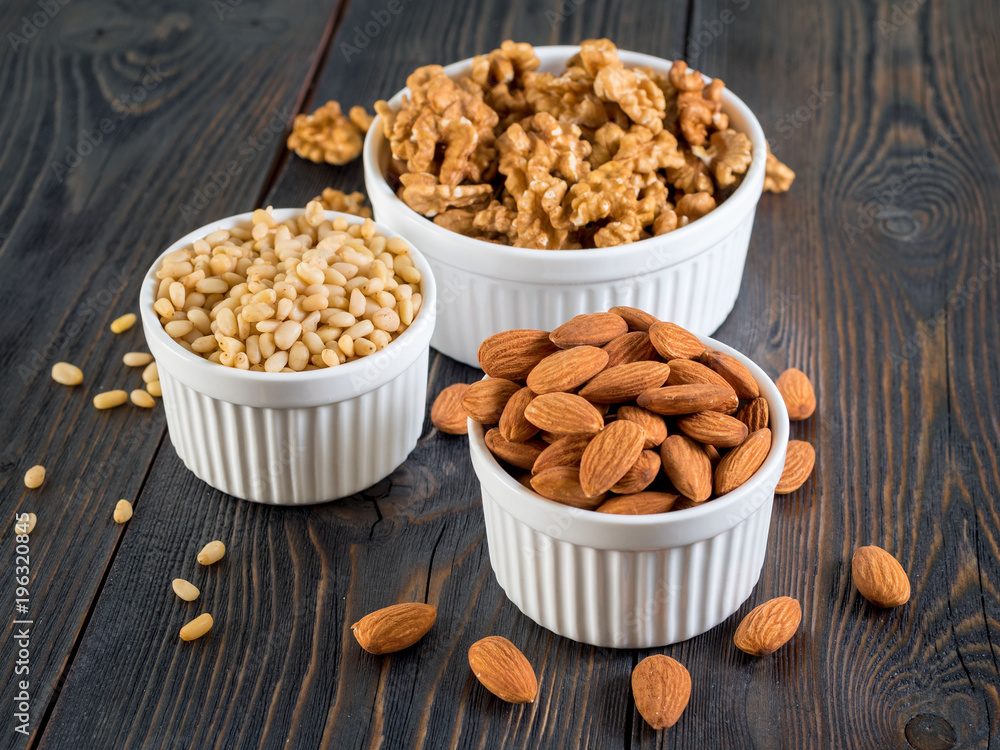 assorted nuts in white bowl on wooden dark background, mix of walnuts, almonds and cedar, side view assorted nuts in white bowl on wooden dark background, mix of walnuts, almonds and cedar, side view