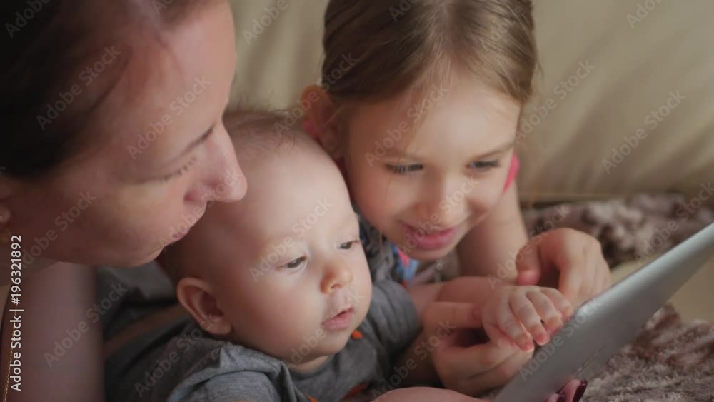 Mother and children with a tablet computer at home watching cartoons and playing. Mother and children with a tablet computer at home watching cartoons and playing.