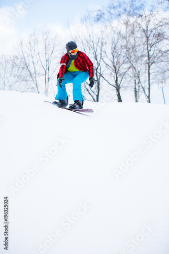 Picture of athlete in checked shirt with snowboard riding in snowy resort