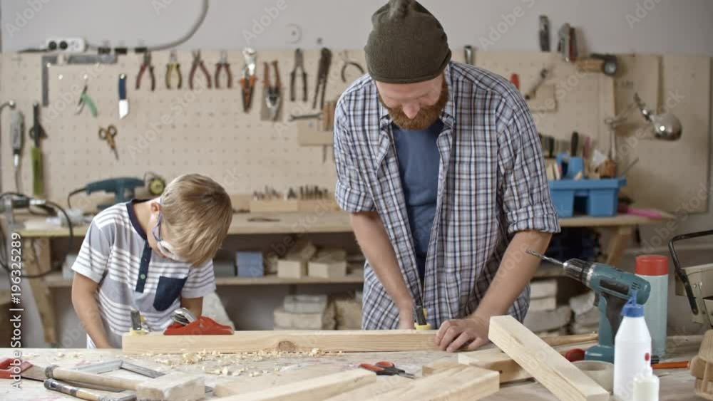Father and son working in art studio and using clamps to secure wooden block in place before working with it Father and son working in art studio and using clamps to secure wooden block in place before working with it