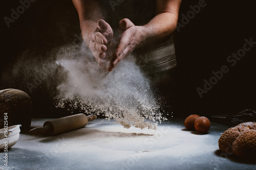 Fotografía hand of chef clap a flour with wooden rolling pin and ingredients on dark backgr