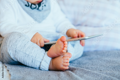 Unrecognizable иarefoot infant baby boy using tablet at home interior. Childern and gadget concept.