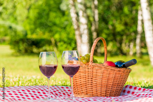 Fototapeta Naklejka Na Ścianę i Meble -  wicker basket for a picnic with fruit and red wine on a tablecloth in a park for two lovers