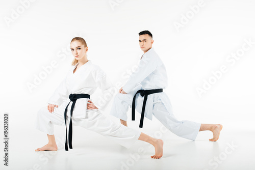 karate fighters stretching legs and looking at camera isolated on white