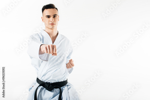 male karate fighter performing hit and looking at camera isolated on white