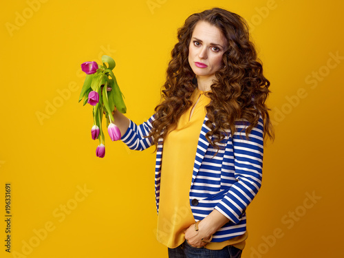 unhappy woman against yellow background showing wilted flowers
