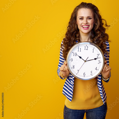 smiling young woman against yellow background showing clock